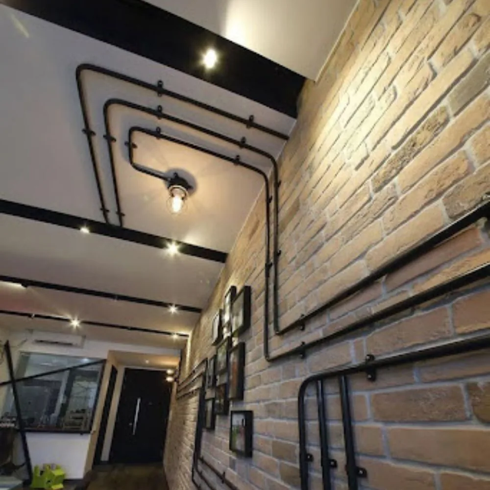 Exposed black conduit runs along a brick wall and ceiling with ceiling light fixtures