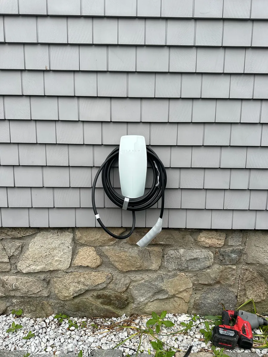 Tesla wall connector EV charger mounted on a home exterior wall with its cable coiled