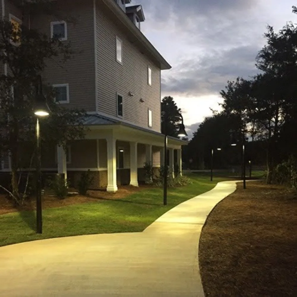 Lit walkway post lights along a path outside a multi-story commercial property at dusk